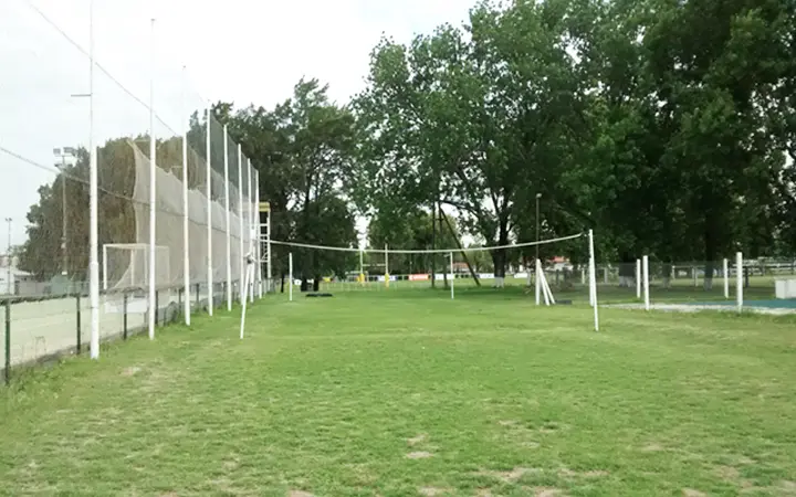 Espacio de pasto con red de vóley y árboles altos