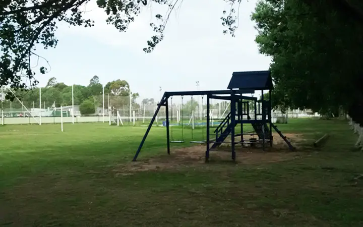 Hamacas y tobogán sobre el pasto con las canchas al fondo