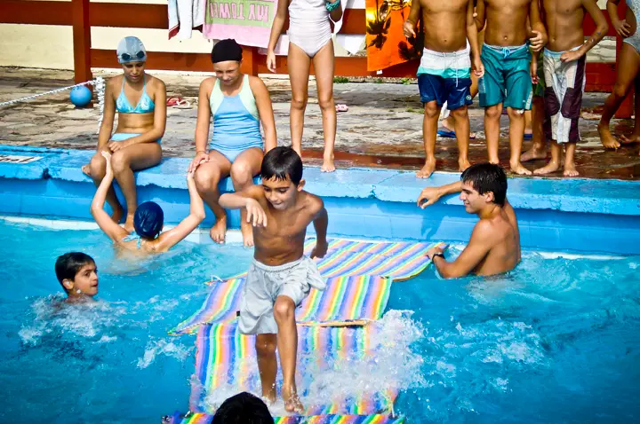 Chicos jugando en la pileta del predio sobre una colchoneta de colores, con un profesor en el agua