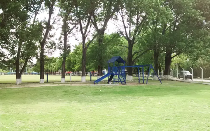 Juegos infantiles azules sobre el pasto, a la sombra de los árboles del predio